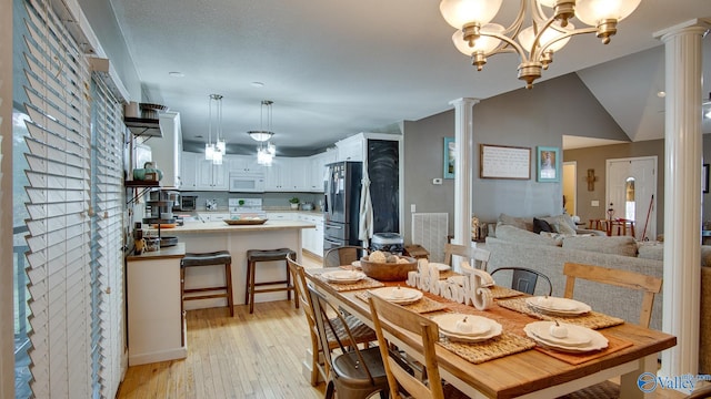 dining space featuring vaulted ceiling, decorative columns, light hardwood / wood-style flooring, and a notable chandelier