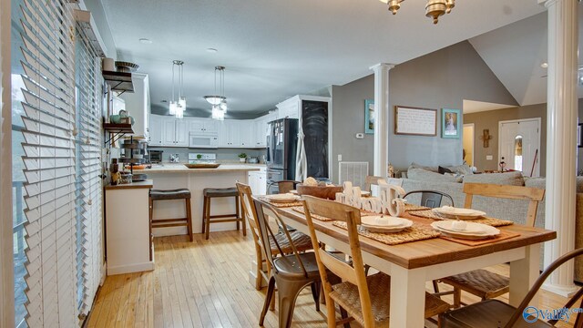 dining area with decorative columns, light hardwood / wood-style flooring, vaulted ceiling, and an inviting chandelier