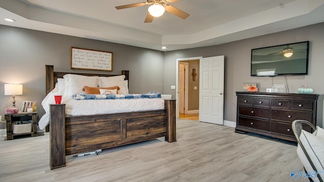 bedroom featuring a raised ceiling, ceiling fan, and light wood-type flooring