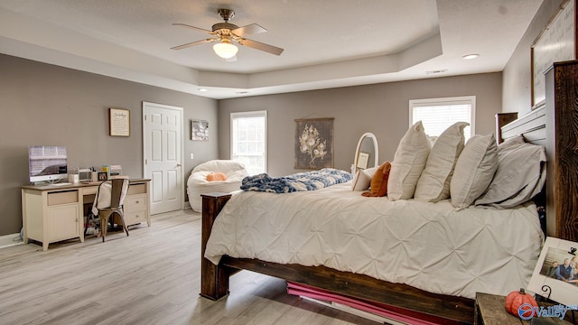 bedroom featuring ceiling fan, a raised ceiling, and light wood-type flooring