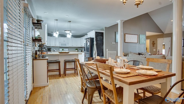 dining room featuring light hardwood / wood-style floors, decorative columns, and vaulted ceiling