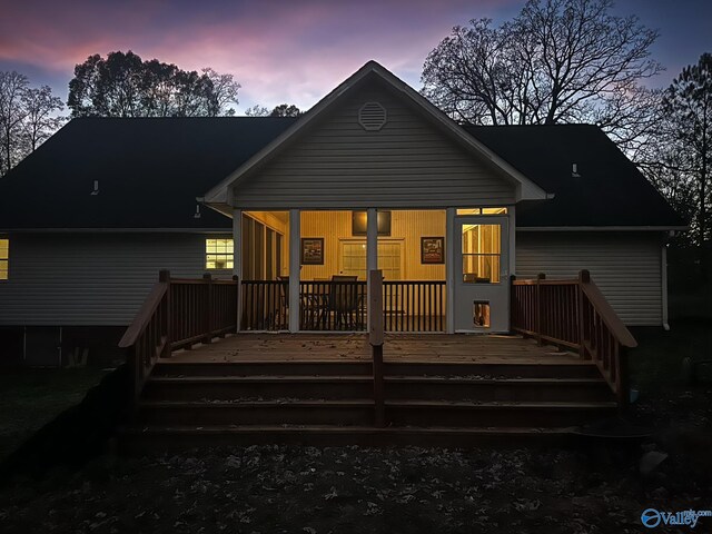 back house at dusk featuring a sunroom and a deck