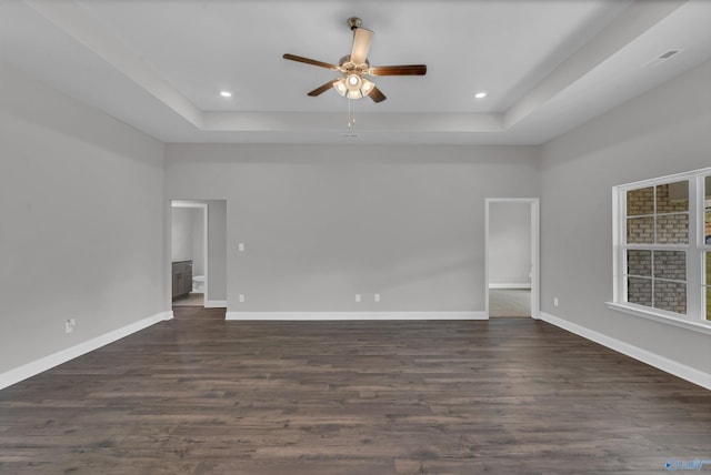 empty room with a raised ceiling, ceiling fan, and dark hardwood / wood-style flooring