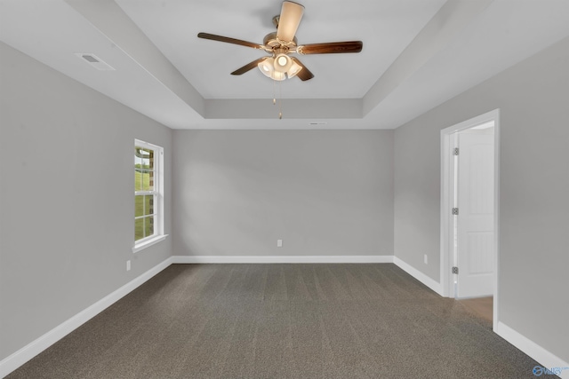 unfurnished room with ceiling fan, a tray ceiling, and dark colored carpet