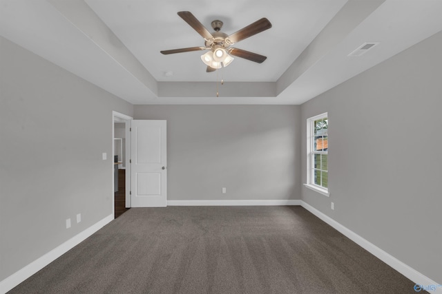 unfurnished room with ceiling fan, dark colored carpet, and a raised ceiling