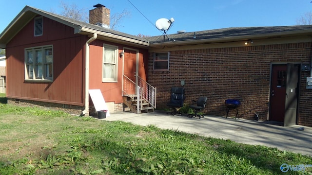 back of house featuring entry steps, a lawn, a patio, a chimney, and brick siding