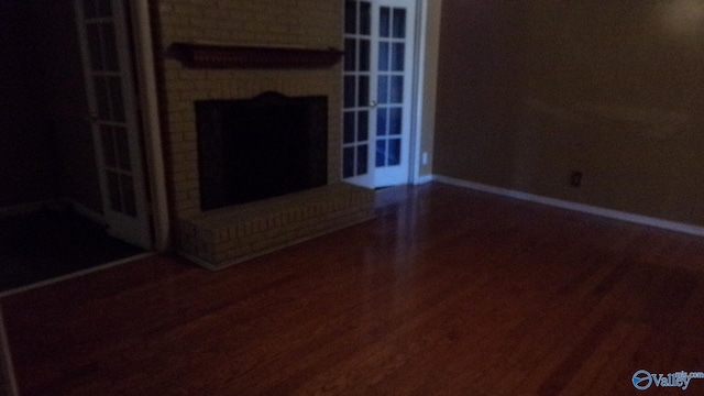 unfurnished living room with a brick fireplace, wood finished floors, and baseboards