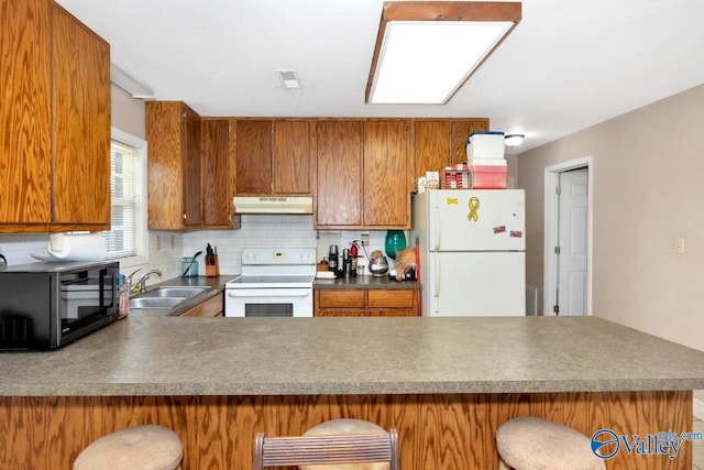 kitchen with a sink, a peninsula, under cabinet range hood, white appliances, and visible vents