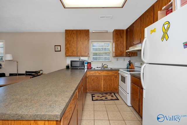 kitchen featuring white appliances, under cabinet range hood, dark countertops, visible vents, and a peninsula
