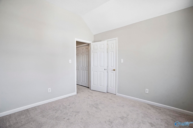 unfurnished bedroom featuring light carpet, baseboards, and vaulted ceiling