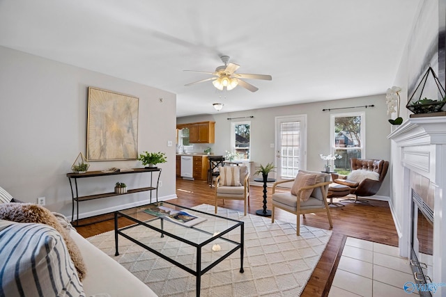 living room with ceiling fan, light wood-style floors, baseboards, and a tile fireplace