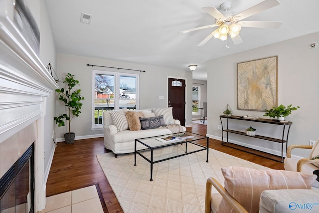 living area featuring wood finished floors, visible vents, baseboards, ceiling fan, and a glass covered fireplace