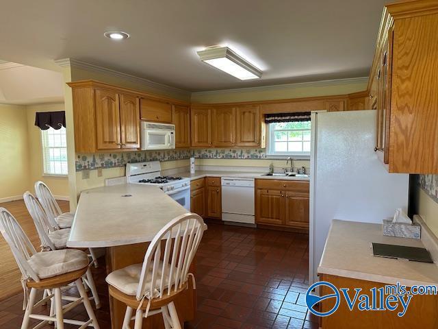 kitchen with light countertops, a sink, white appliances, brick floor, and a breakfast bar area