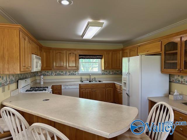 kitchen featuring a kitchen breakfast bar, light countertops, a sink, white appliances, and a peninsula