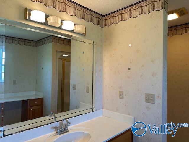 bathroom featuring wallpapered walls, vanity, and a textured ceiling