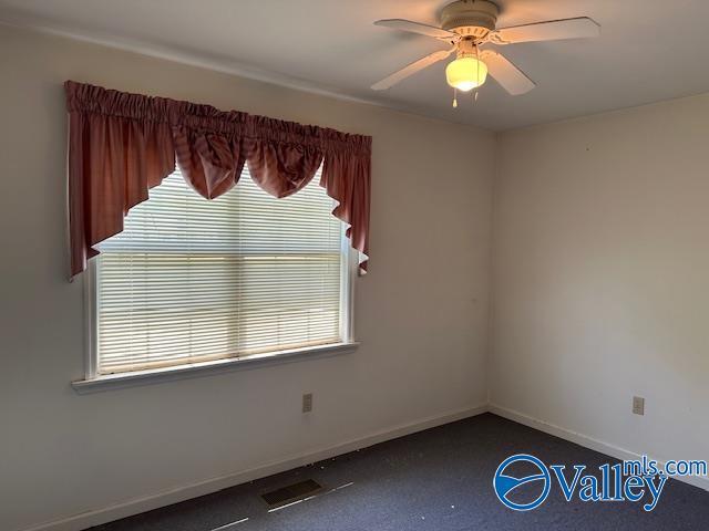 spare room featuring dark colored carpet, a wealth of natural light, baseboards, and ceiling fan