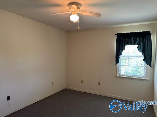 spare room featuring dark carpet and ceiling fan