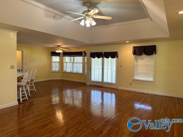 unfurnished living room with baseboards, a ceiling fan, wood finished floors, and a tray ceiling