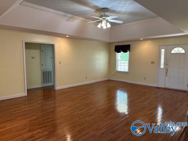 unfurnished living room featuring a tray ceiling, baseboards, visible vents, a ceiling fan, and wood finished floors