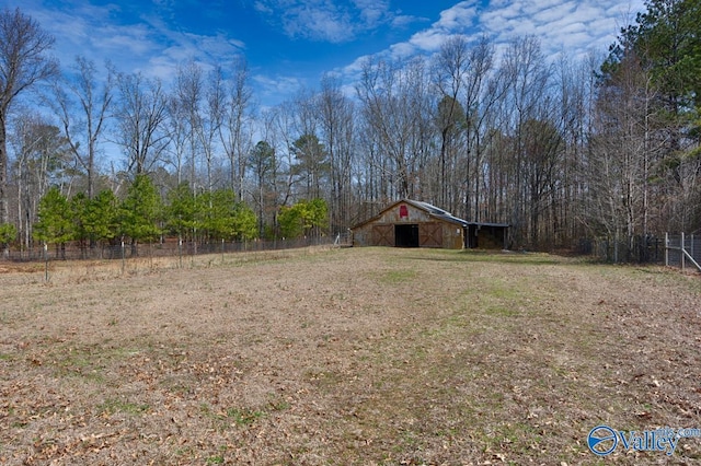 view of yard featuring an outbuilding, fence, a barn, and a wooded view