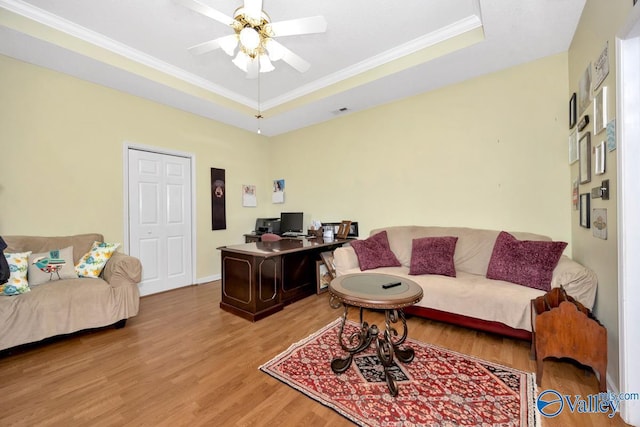 office space with baseboards, ceiling fan, wood finished floors, a tray ceiling, and crown molding