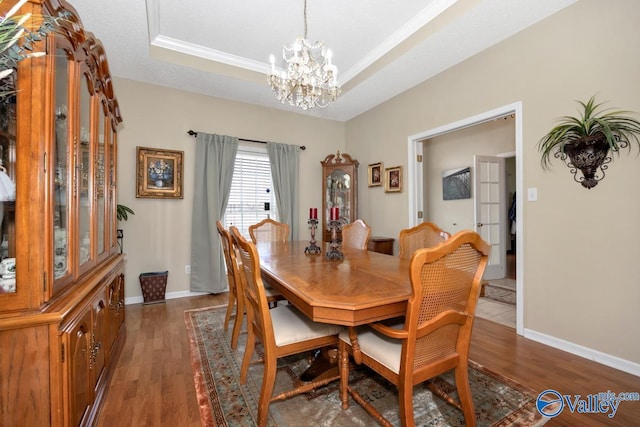 dining space featuring a chandelier, wood finished floors, a raised ceiling, and baseboards