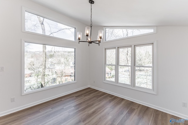 unfurnished dining area featuring dark wood-style floors, a chandelier, vaulted ceiling, and baseboards