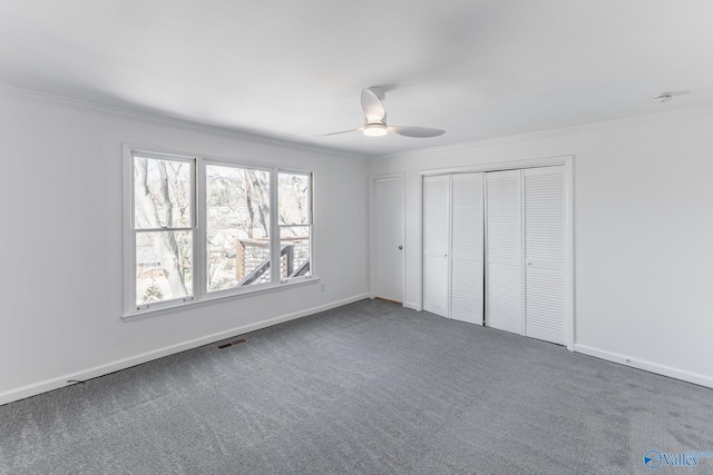 unfurnished bedroom with baseboards, visible vents, dark colored carpet, and crown molding