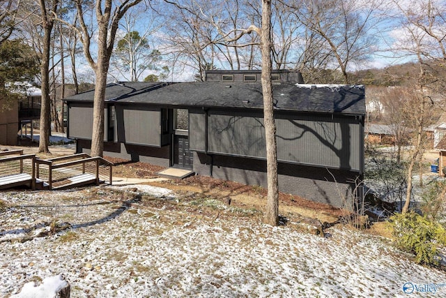 snow covered property with roof with shingles and brick siding