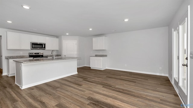 kitchen with appliances with stainless steel finishes, white cabinetry, light stone countertops, a center island with sink, and dark hardwood / wood-style flooring