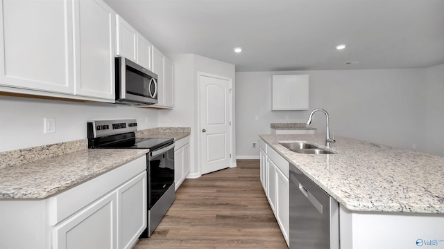 kitchen featuring appliances with stainless steel finishes, an island with sink, sink, white cabinets, and light stone counters