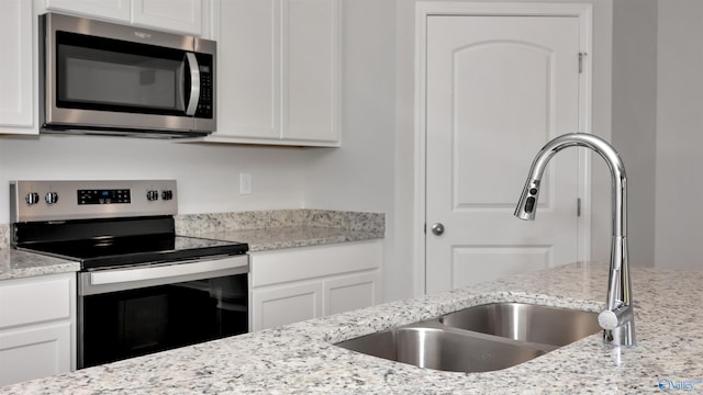 kitchen with appliances with stainless steel finishes, sink, white cabinets, and light stone counters