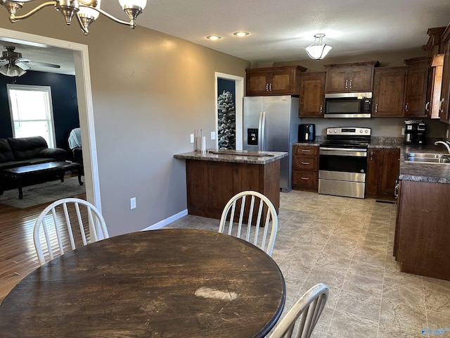 kitchen featuring dark brown cabinetry, sink, stainless steel appliances, kitchen peninsula, and ceiling fan with notable chandelier