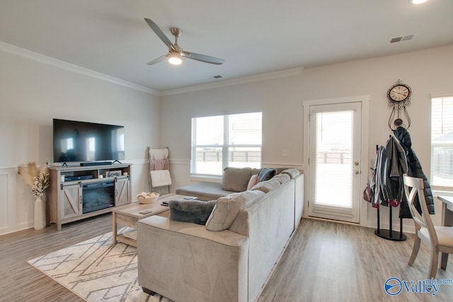 living room with light wood-type flooring, a healthy amount of sunlight, and crown molding