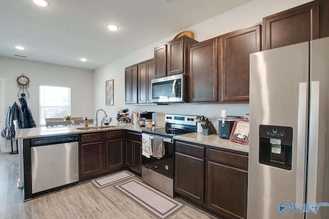 kitchen featuring sink, light hardwood / wood-style flooring, kitchen peninsula, dark brown cabinetry, and appliances with stainless steel finishes