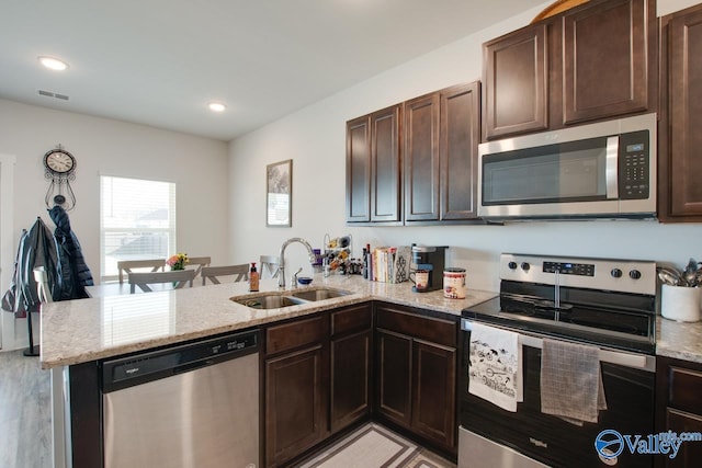 kitchen with kitchen peninsula, light stone countertops, appliances with stainless steel finishes, dark brown cabinets, and sink