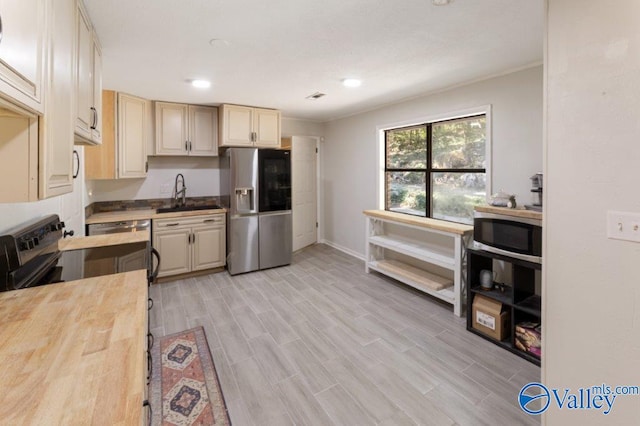 kitchen with a sink, baseboards, light wood-style floors, wood counters, and appliances with stainless steel finishes
