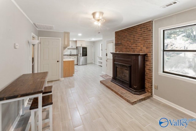 unfurnished living room featuring light wood finished floors, visible vents, a ceiling fan, and a sink