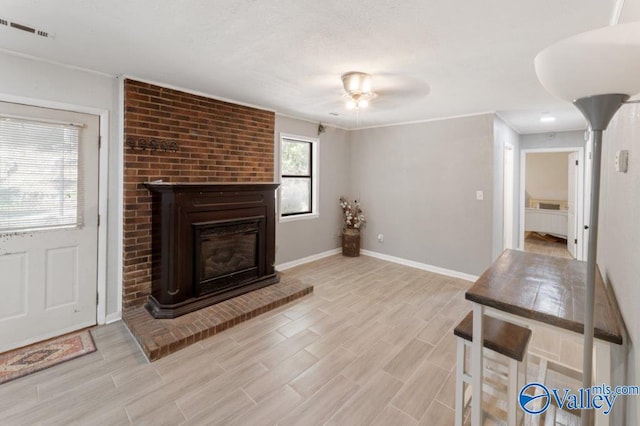 living room with visible vents, a ceiling fan, baseboards, light wood-style flooring, and a brick fireplace