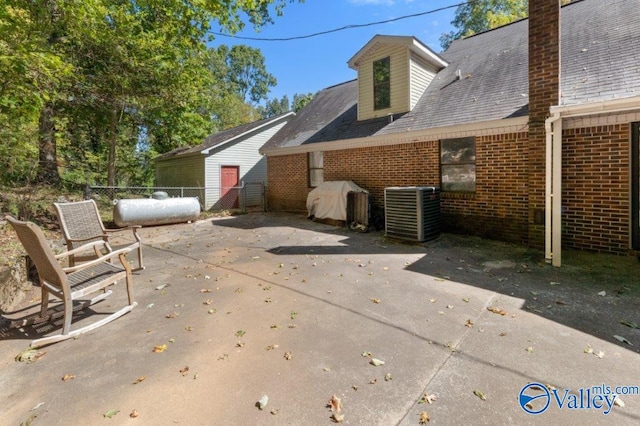 exterior space with roof with shingles, central AC, fence, brick siding, and a patio area