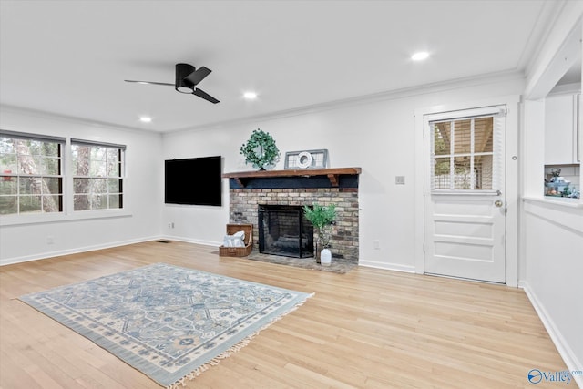 living room featuring a fireplace, ornamental molding, a ceiling fan, light wood-type flooring, and baseboards