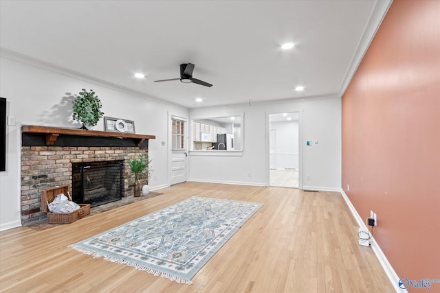 living area with crown molding, a brick fireplace, ceiling fan, wood finished floors, and baseboards