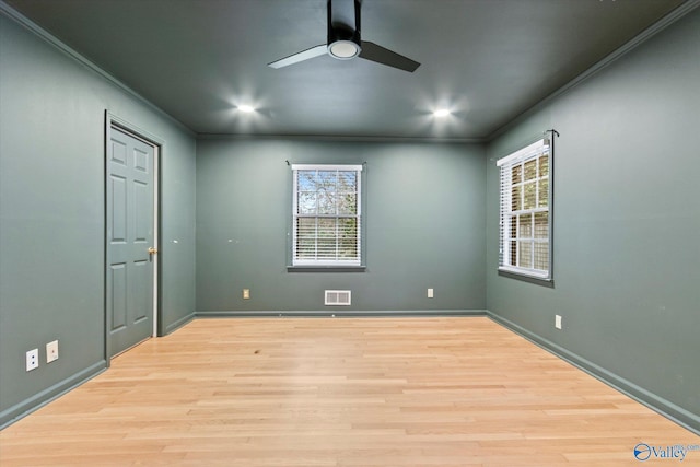 empty room with light wood-type flooring, ornamental molding, plenty of natural light, and visible vents