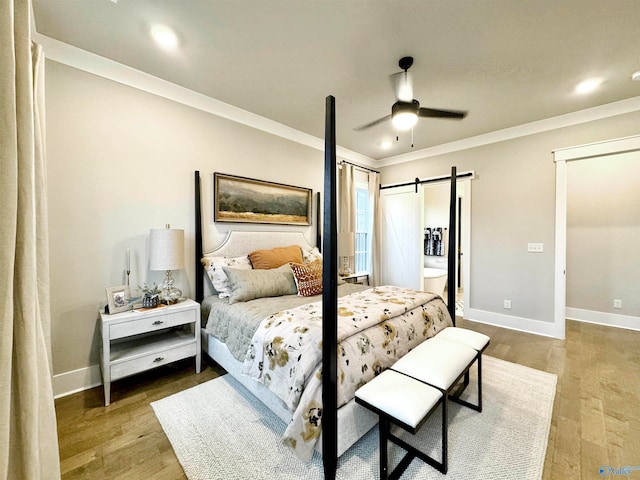 bedroom with hardwood / wood-style flooring, crown molding, a barn door, and ceiling fan