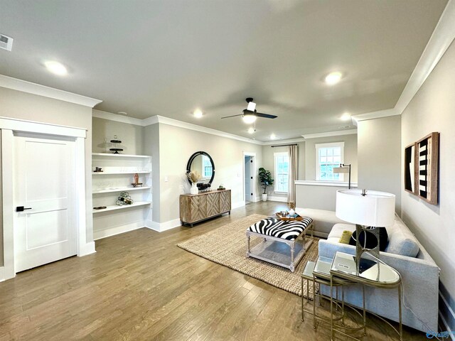 living room with wood-type flooring, built in shelves, ornamental molding, and ceiling fan