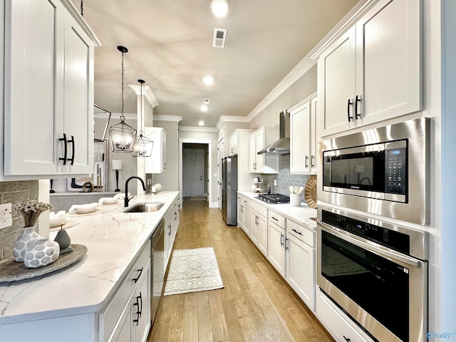 kitchen with stainless steel appliances, decorative backsplash, light wood-type flooring, wall chimney exhaust hood, and light stone counters