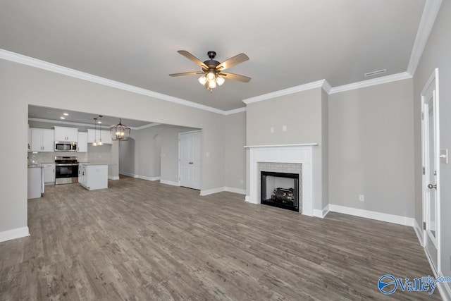 unfurnished living room featuring ceiling fan with notable chandelier, hardwood / wood-style flooring, a brick fireplace, and crown molding