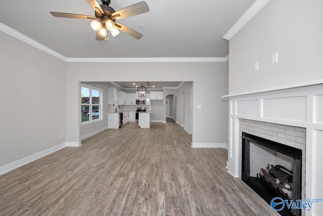 unfurnished living room with light hardwood / wood-style floors, a brick fireplace, ceiling fan, and crown molding