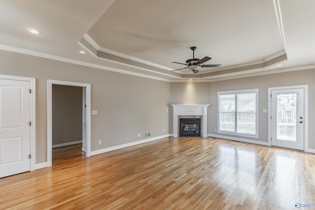 unfurnished living room featuring a tray ceiling, ceiling fan, crown molding, and light wood-type flooring