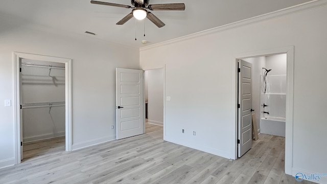 unfurnished bedroom featuring visible vents, ornamental molding, a walk in closet, light wood-style floors, and a closet